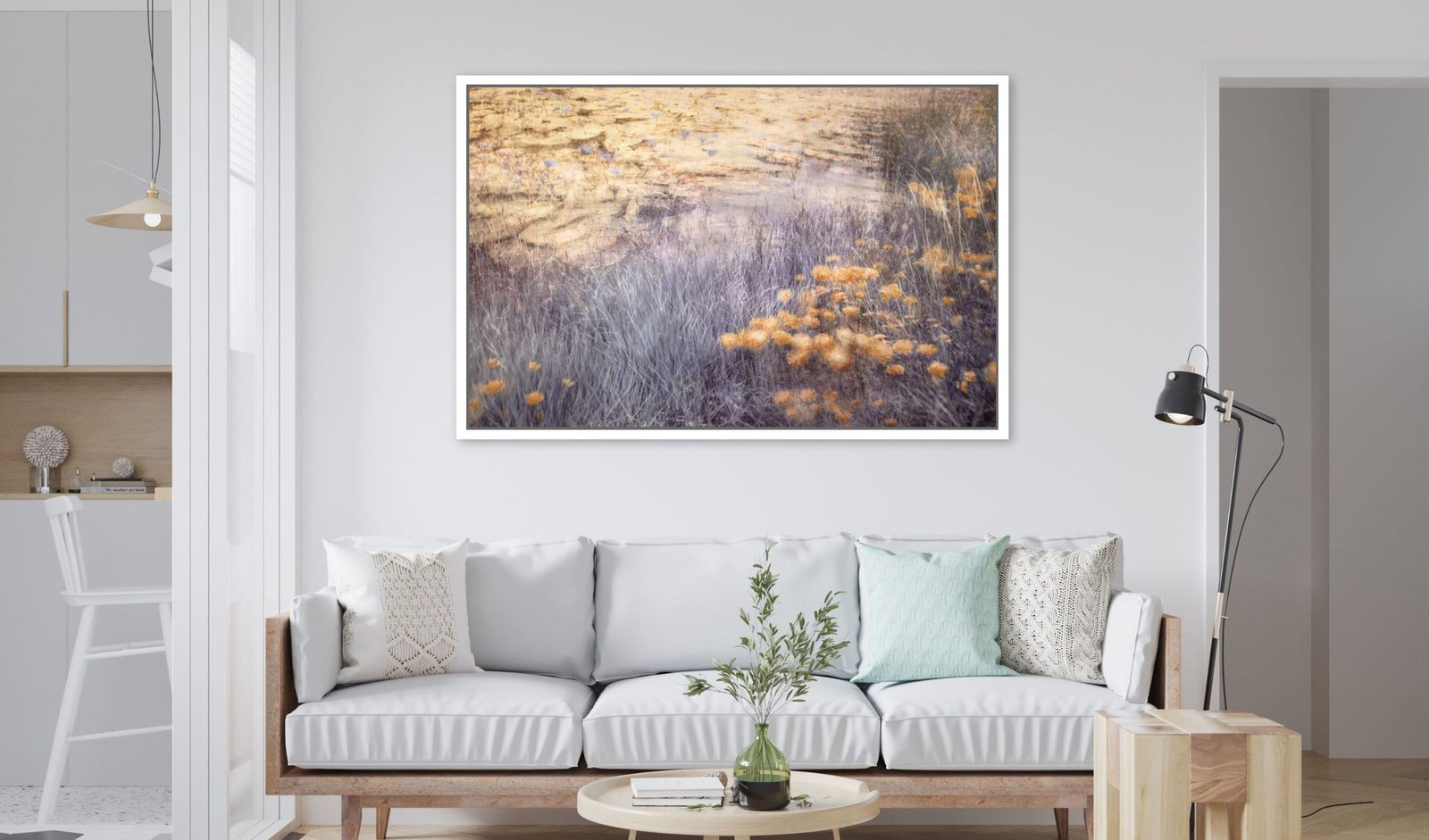 A landscape artwork in a natural wood frame above a white sofa