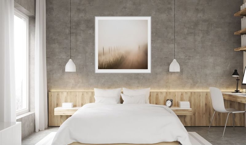 Square misty grassland print in a white frame above a bed