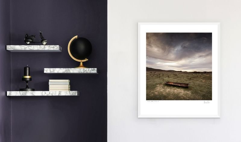 Stormy field landscape in a white frame beside dark shelving